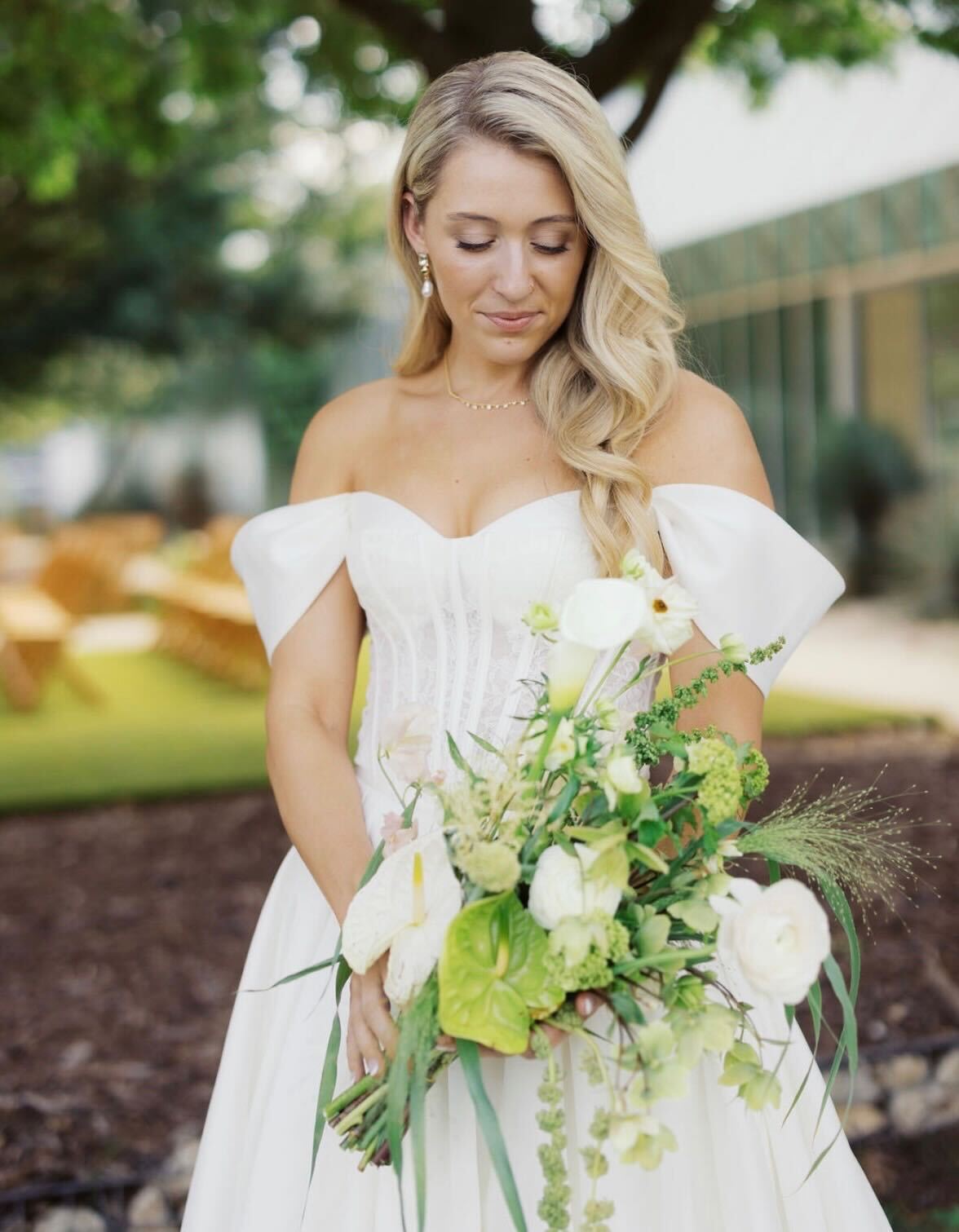 Bride in an off-shoulder corset gown holding a textural ivory bouquet with calla lilies and trailing greens